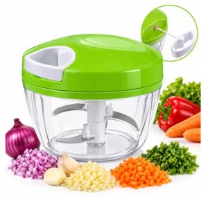 Green Manual Vegetable Chopper with a Clear Bowl and Stainless Blades, Shown with Chopped Onions, Garlic, Carrot, and Herbs Nearby to Suggest Use for Prepping Vegetables.
