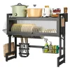 Kitchen Dish Drying Rack with Dishes on the Upper Rack, Utensils Hanging Below, and a Basket of Cleaning Supplies on the Side.
